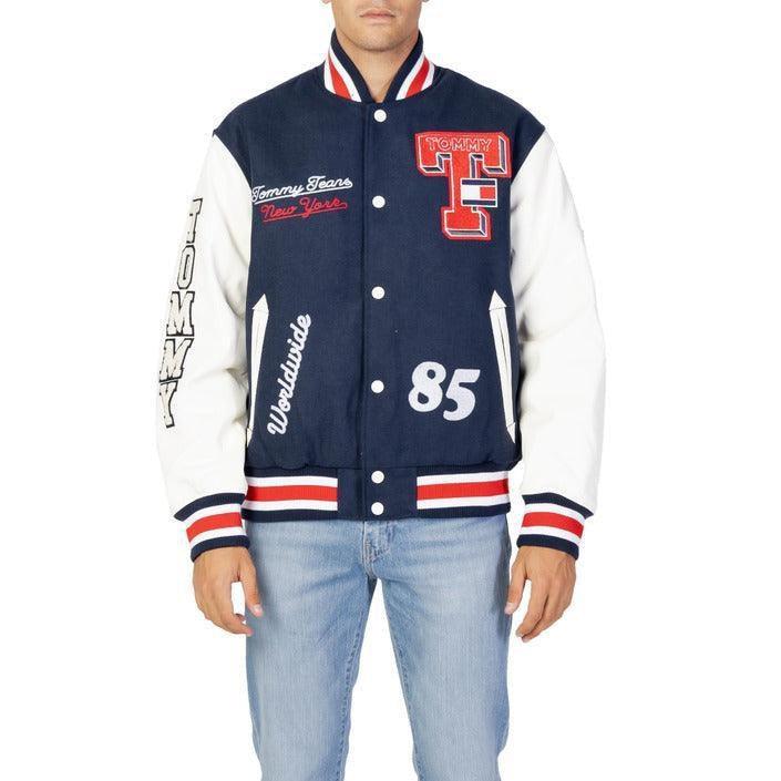 Man wearing navy blue and white varsity jacket with Tommy Jeans patches and blue jeans