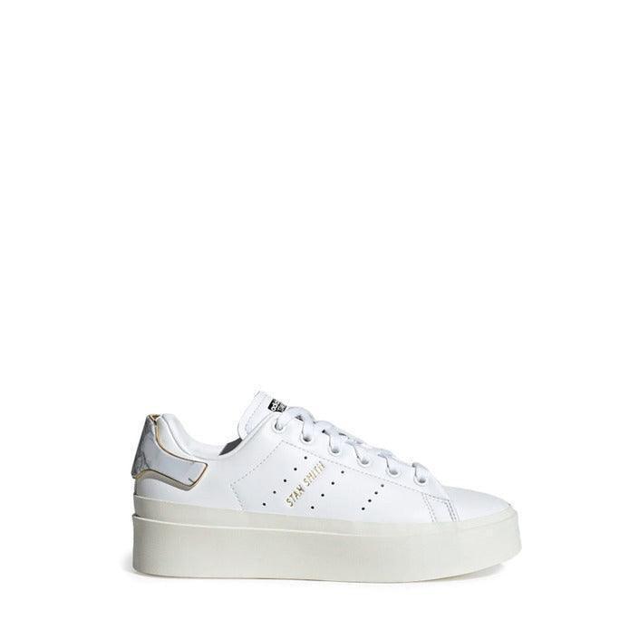 White women's sneaker with thick sole and gold accent, product photo on white background