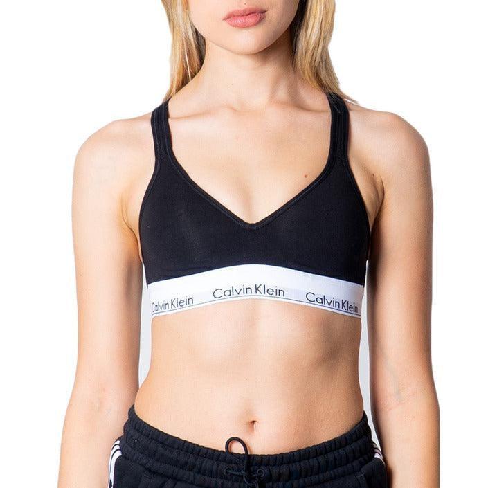 Woman wearing black Calvin Klein sports bra and black pants, posing against white background