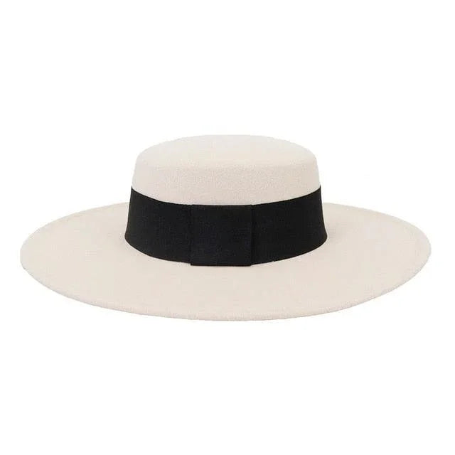 Beige derby fedora hat with wide black band and flat brim on white background