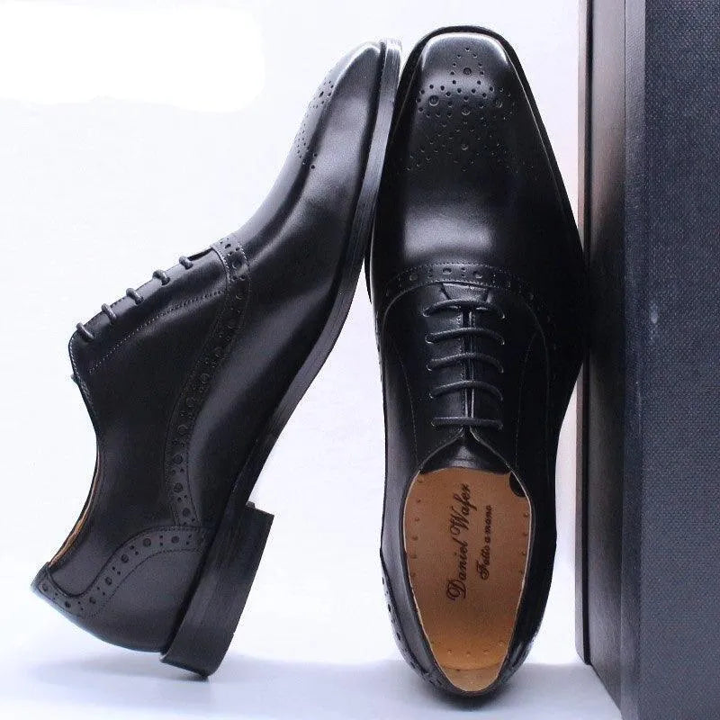 Black leather lace-up men's dress shoes with brogue detailing on a light background