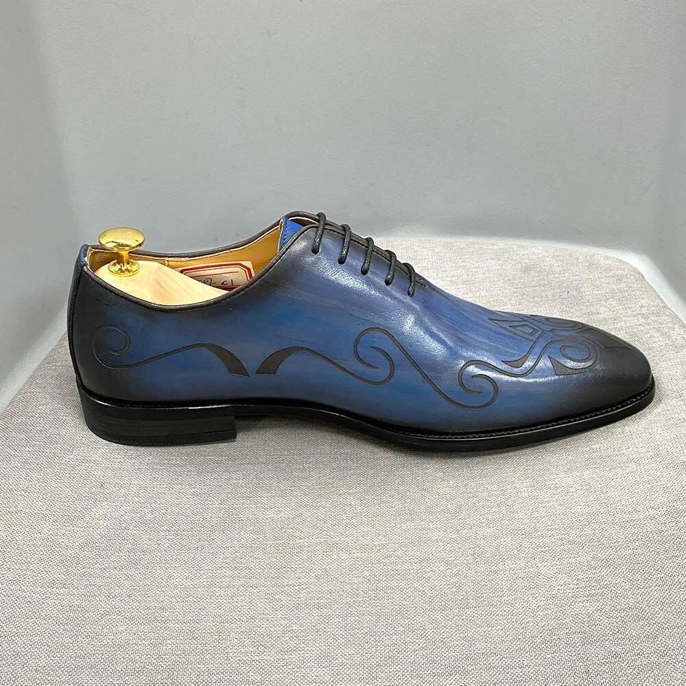 Blue leather men's dress shoe with black swirl design on a gray fabric surface