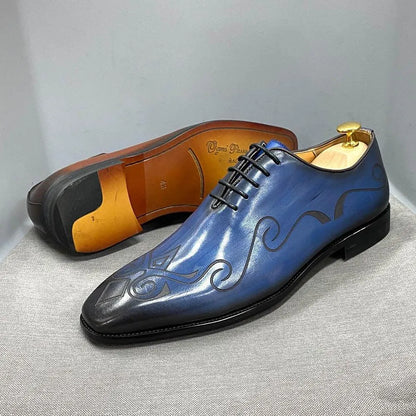 Blue leather men's dress shoes with black swirl design on gray background