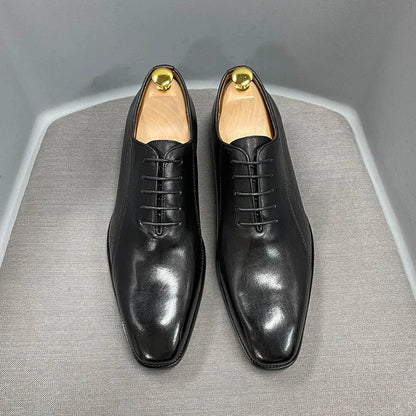 Black leather men's dress shoes with wooden shoe trees on a gray chair