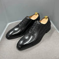 Black leather men's dress shoes with laces on a gray surface, shoe trees inserted
