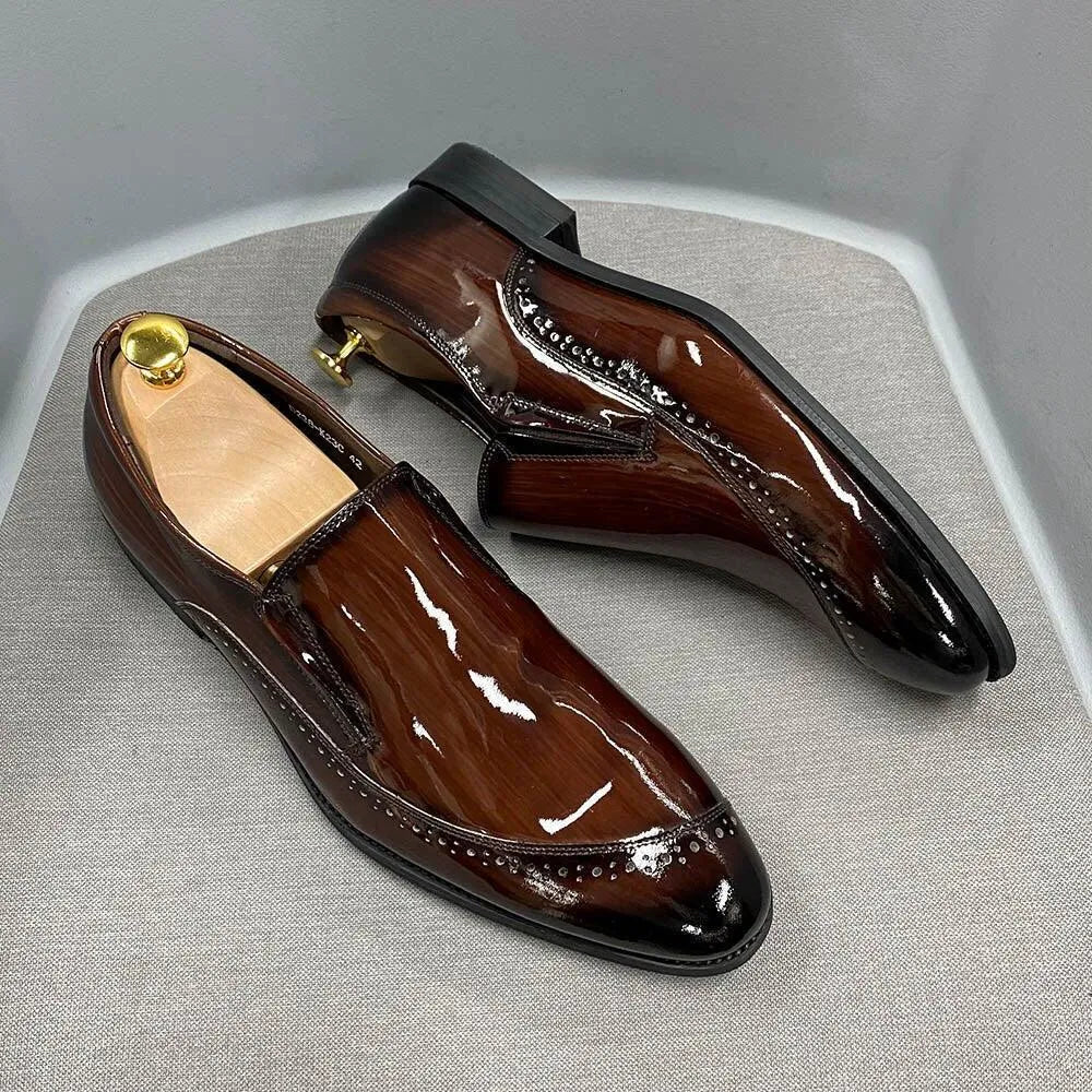 Glossy brown slip-on men's dress shoes with brogue detailing on a light fabric surface