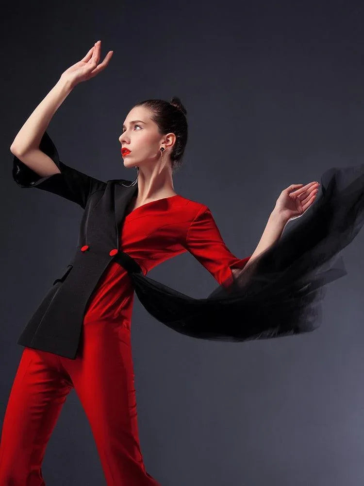 Woman modeling red and black pantsuit with flowing detachable veil against dark background